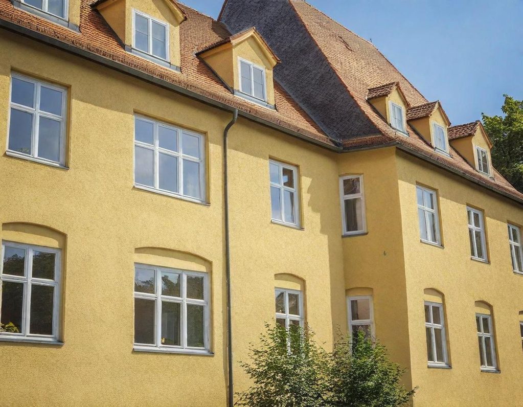 Gelbes Gebäude Gelbes Gebäude mit vielen Fenstern und einem steilen Dach, umgeben von Bäumen.